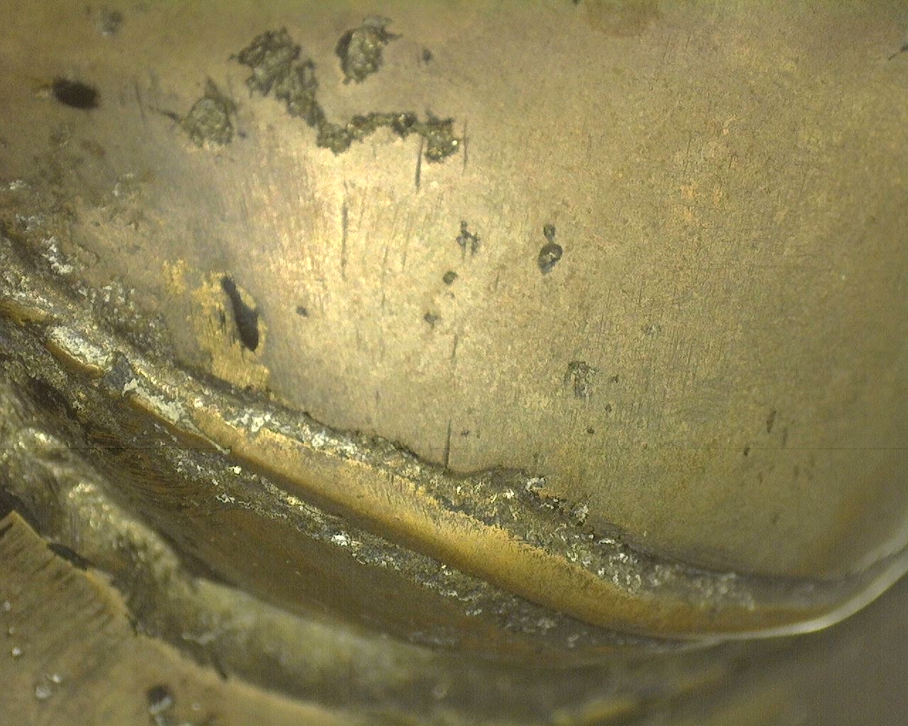 Forensische Makroaufnahme der Messing-Bronze-Gusshaut mit legitimen weißgrauen kristallinen Ablagerungen in den tiefen Einbettungsrändern.