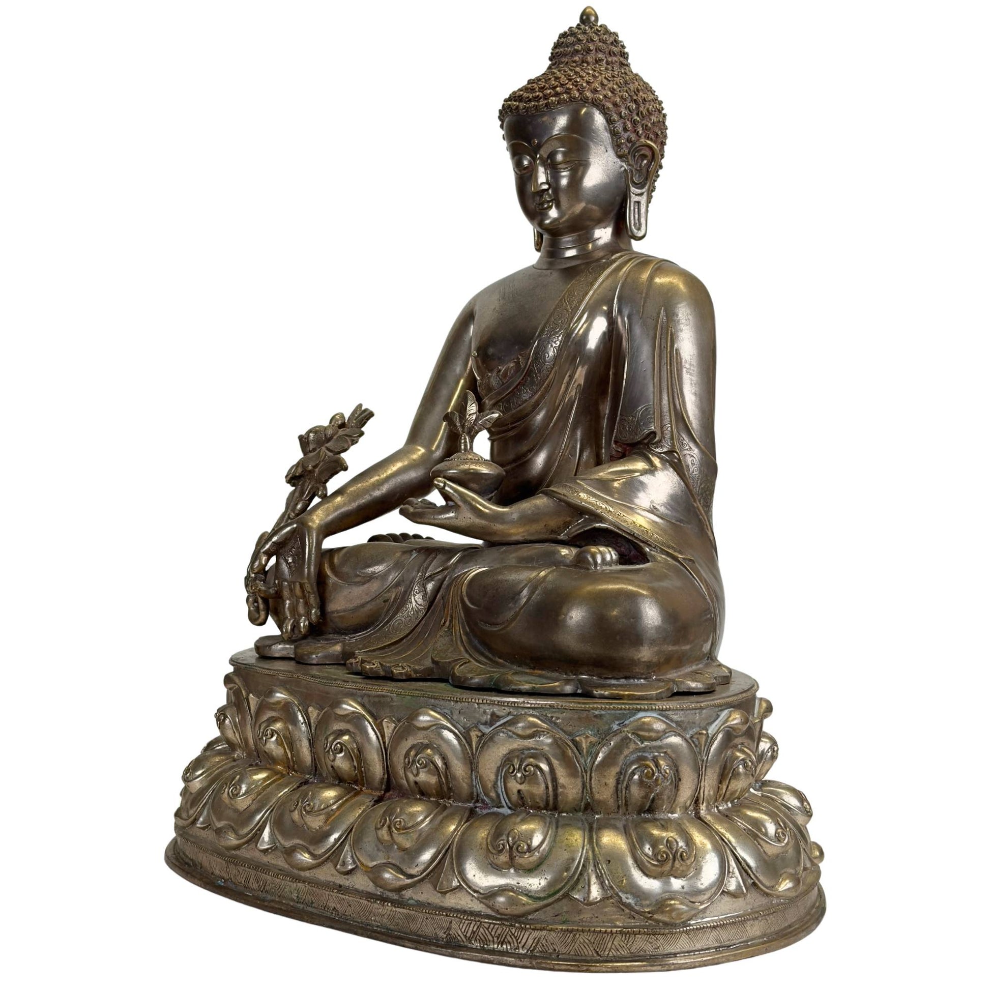 Schräge Vorderansicht eines antiken Newar Bhaisajyaguru aus versilberter Bronze mit Medizintopf, großer Myrobalane, fein gravierten Gewändern, zweiteiligem Lotusthron und natürlicher Patina.